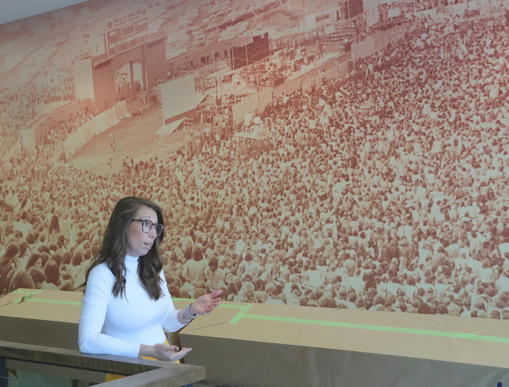 Caitlyn Conley, local history and museum specialist for the Special Collections Division of Akron-Summit County Public Library, discusses the local music scene while standing in front of an Akron History Center mural of the Rolling Stones performing at the Rubber Bowl in 1972. PHIL MASTURZO/AKRON BEACON JOURNAL